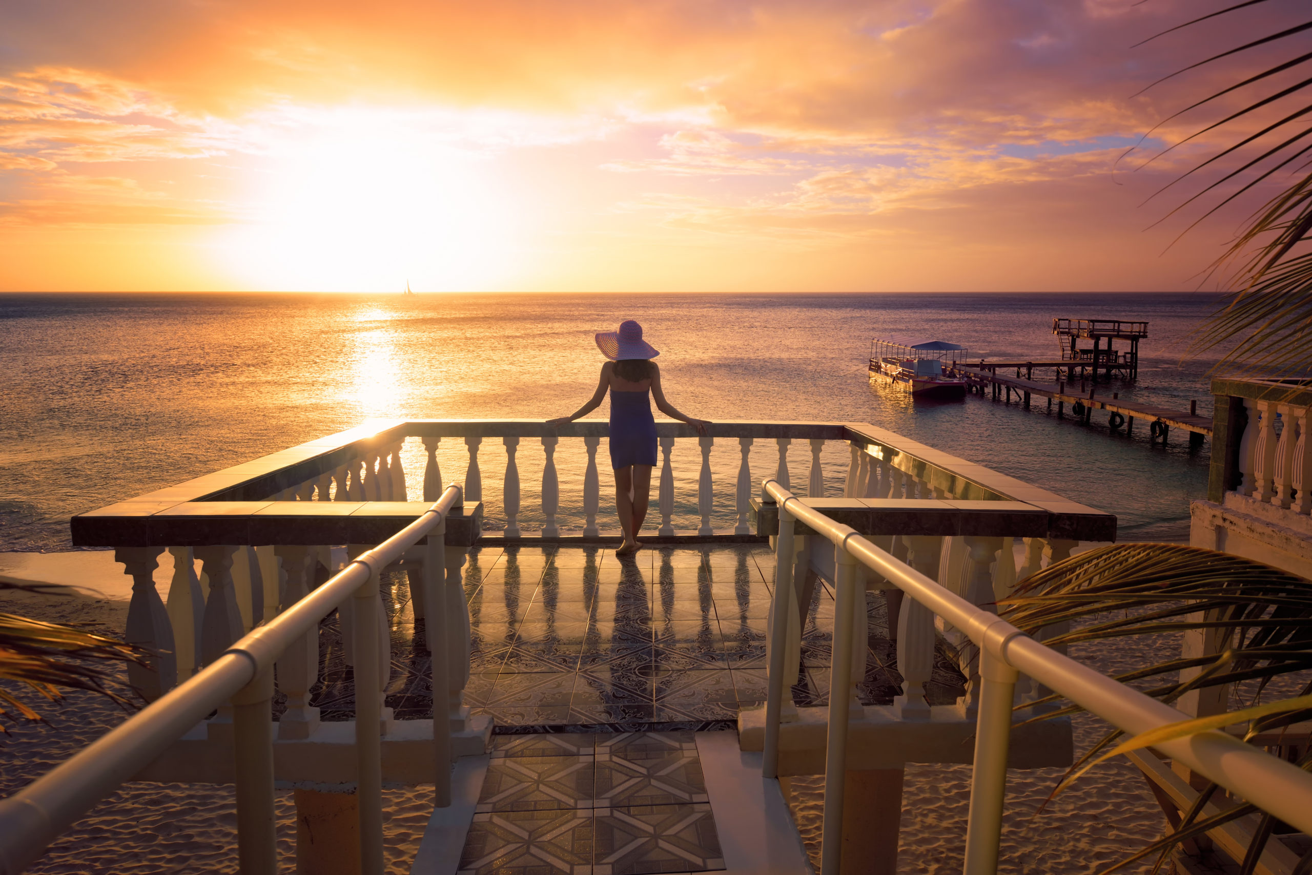 A woman in a hat looking at the romantic Caribbean sunset while